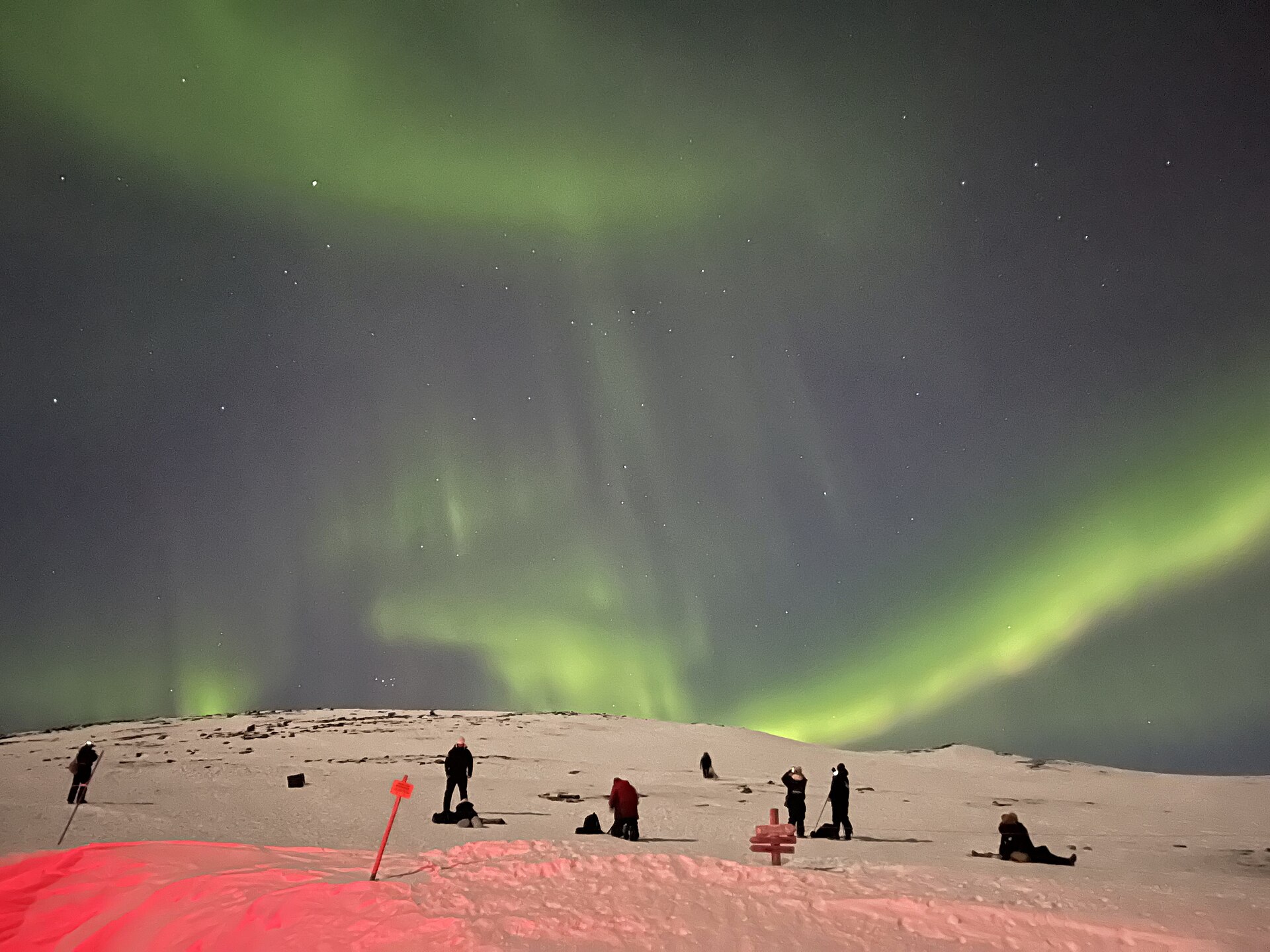 Personas fotografiando la aurora boreal desde una ladera nevada en Abisko