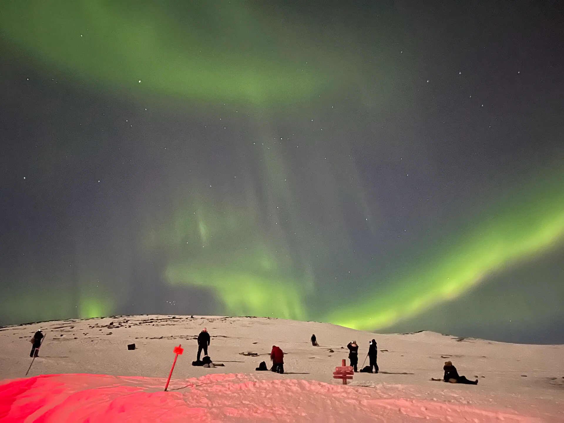 Grupo de personas fotografiando la aurora boreal sobre una ladera nevada en Abisko