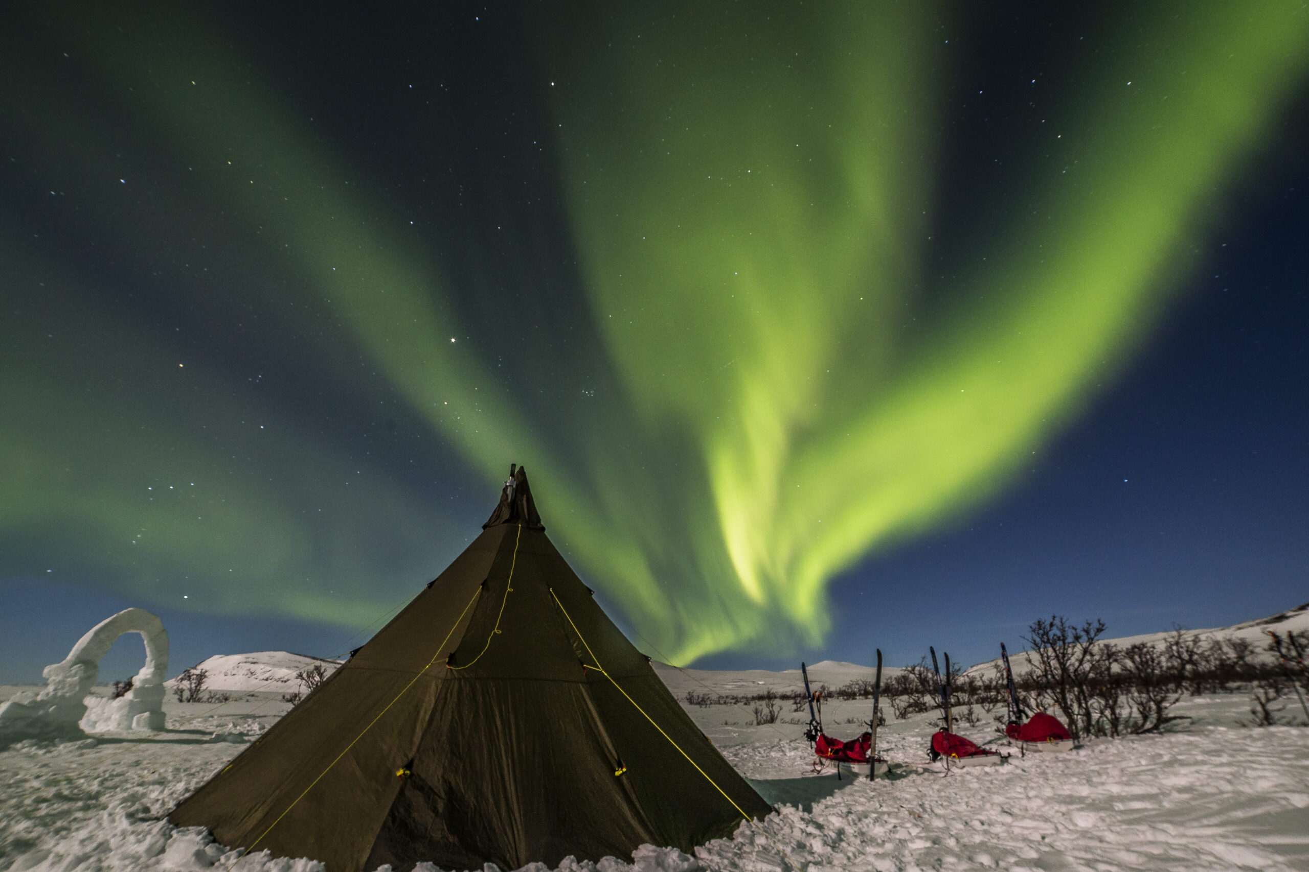 Aurora boreal en arco sobre un tipi iluminado durante una expedición en Laponia