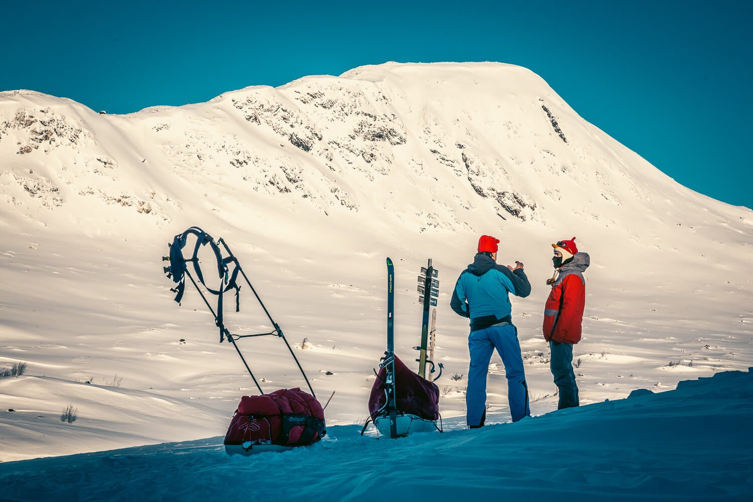 Dos expedicionarios junto a sus pulkas frente a una montaña nevada en Svalbard